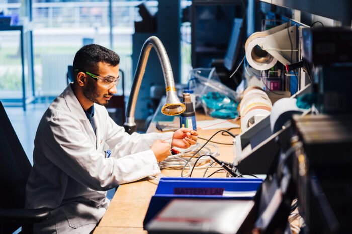 Man in lab coat and goggles pulling role of wire in lab