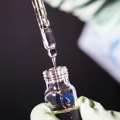 Gloved hand pulling a pipette out of a glass bottle