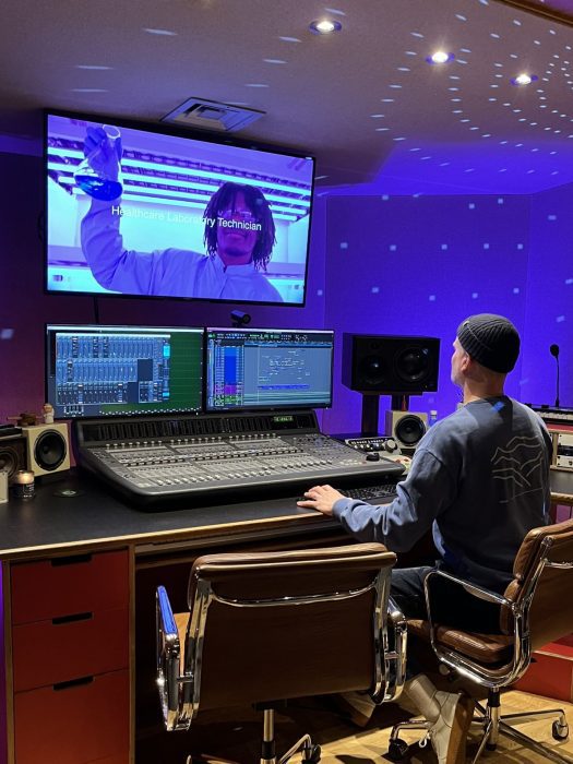 An editor sat in front of several screens, working on a computer and mixing equipment.