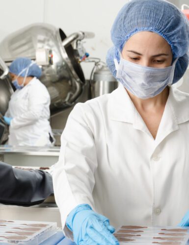 Woman with mask and gloves working on batches of food in factory