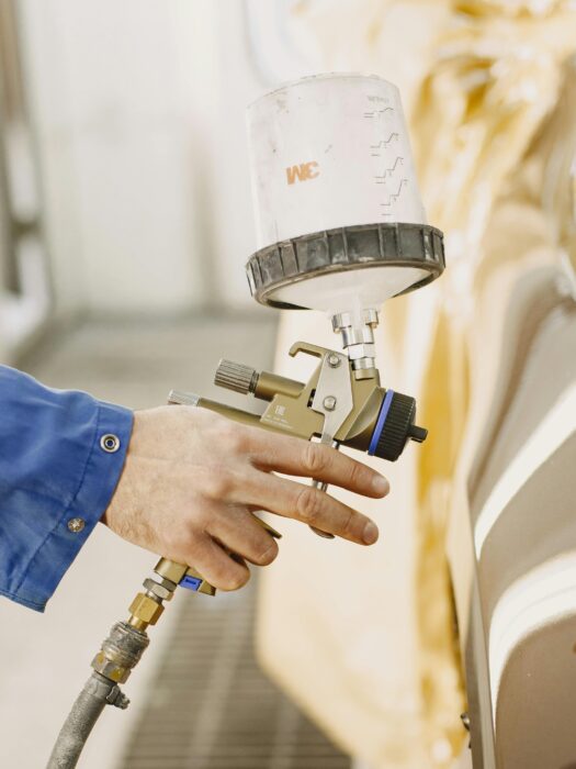 A technician painting a car, using a spray paint gun.