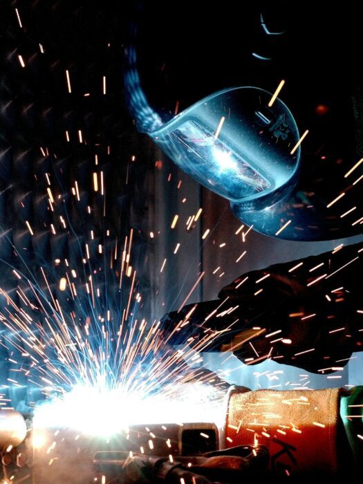 A technician welding, wearing a welder's mask, with sparks flying.
