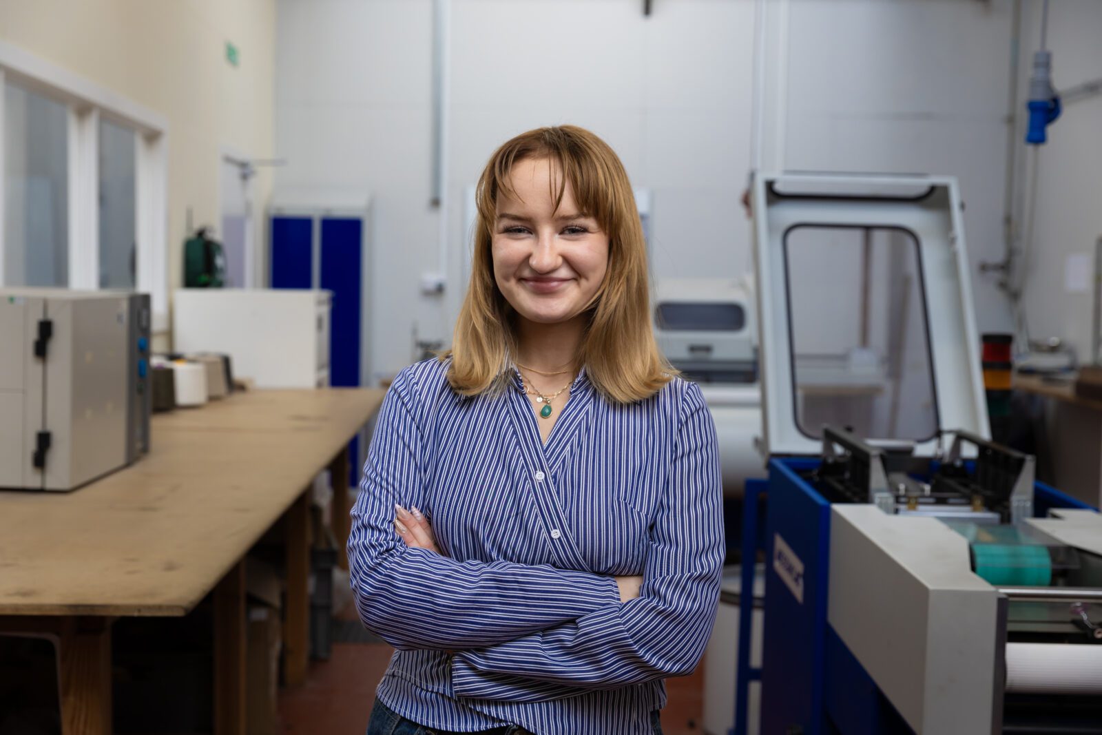 A picture of Amy O'Hare stood in the centre of the frame wearing a blue shirt. She is in a lab.