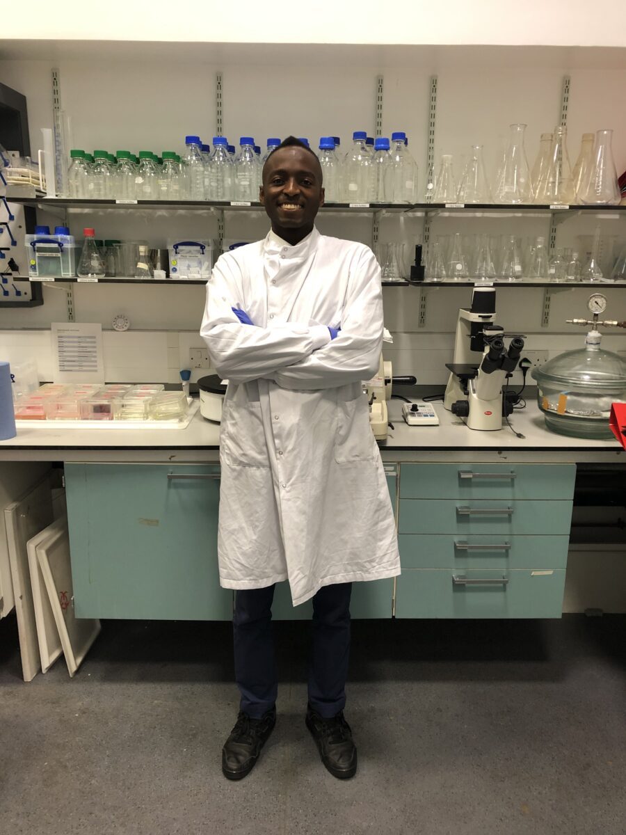 Nana in lab coat in front of bottles in lab