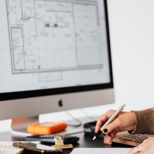 Woman at desk taking notes from a screen showing building plans