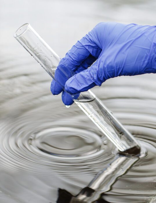 A gloved hand dipping a test tube into water